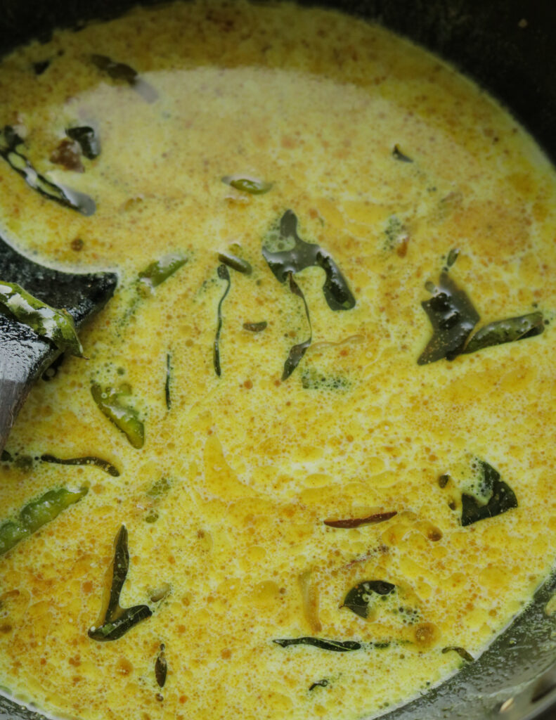 adding coconut milk to the tempered onions, garlic and curry leaves to the egg curry