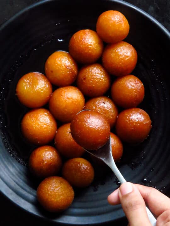 gulab jamuns on a plate with a spoon holding a gulab jamun