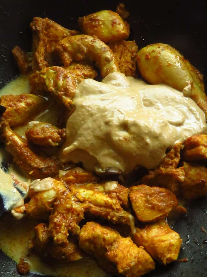 adding yoghurt to the cooking chicken mughlai curry.