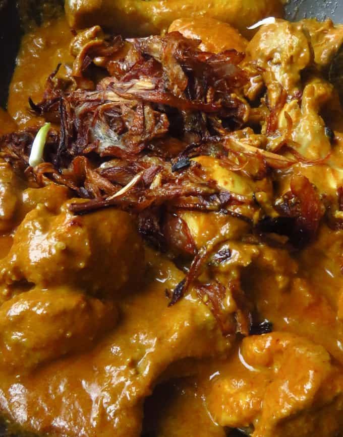 adding fried onions to the cookin mughlai chicken korma recipe.