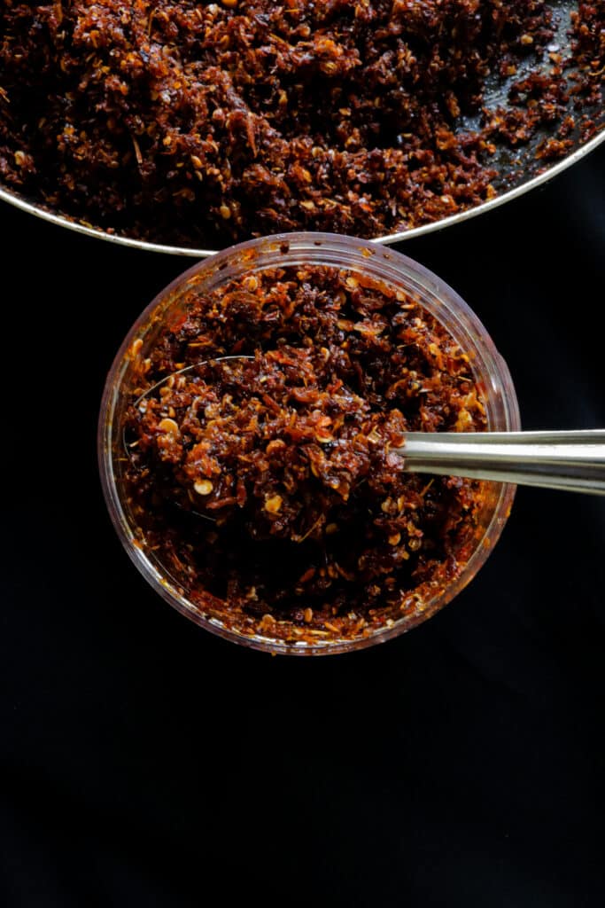 chilli paste in a bowl and bottle scooped with a silver spoon.