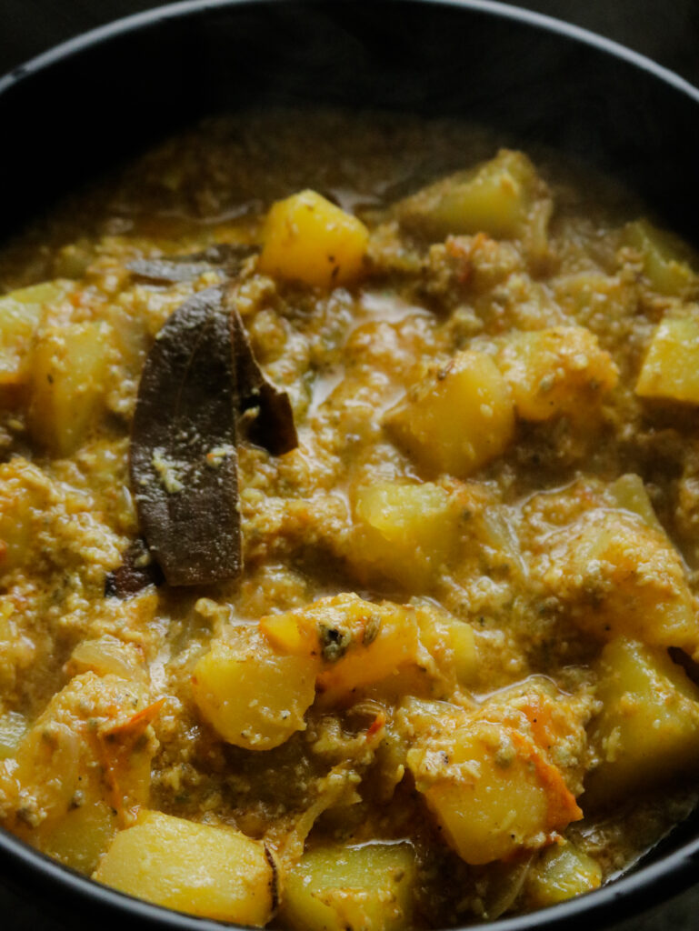 a thick aloo kurma dish served in a black bowl. thick potato curry with bay leaves and spices. 