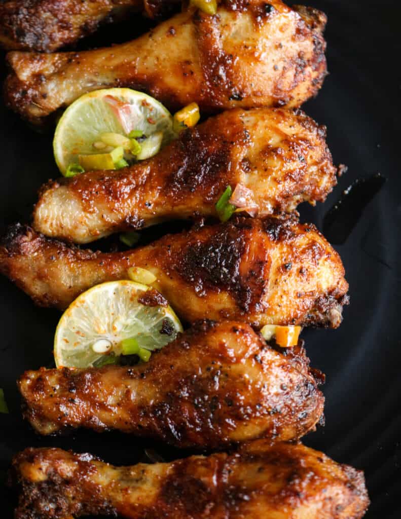 crispy, juicy baked chicken drumsticks with lime slices and placed on a black platter.