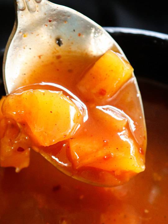 sweet and sour recipe with pineapple chunks scooped in a spoon.