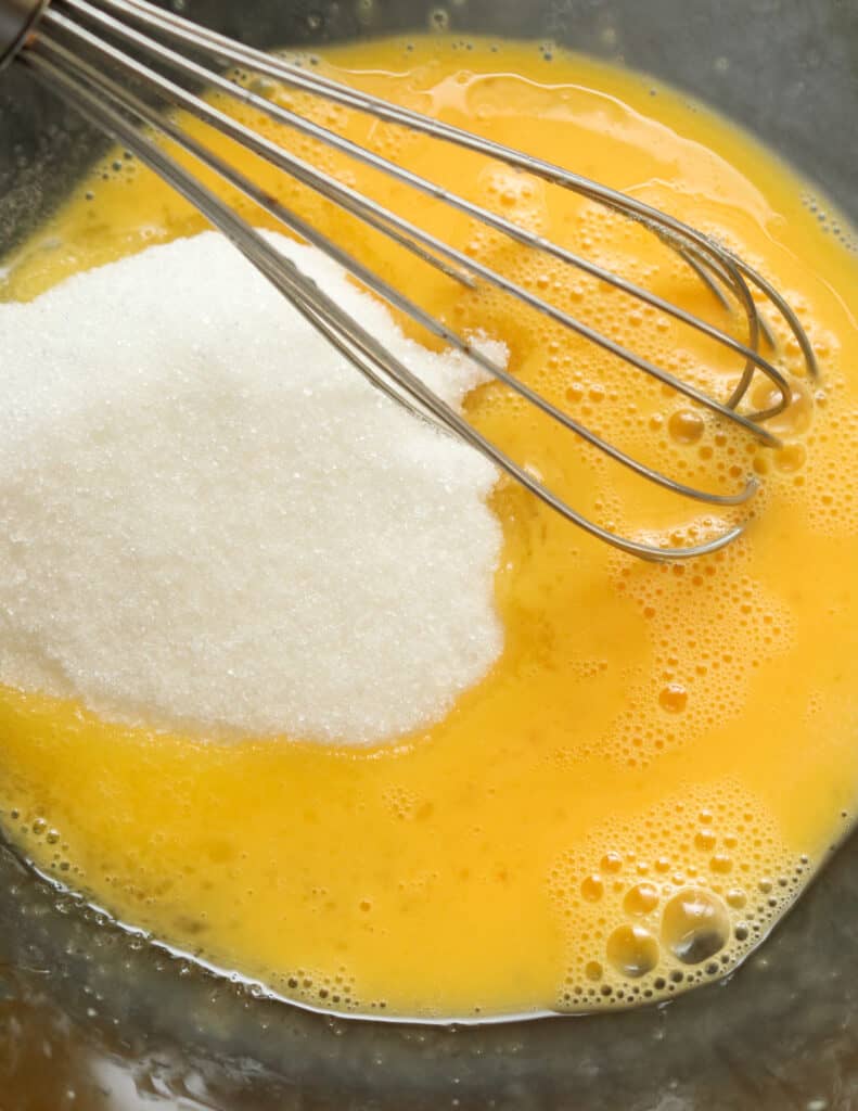 adding sugar to the melted butter and eggs to make the lemon cake slices.