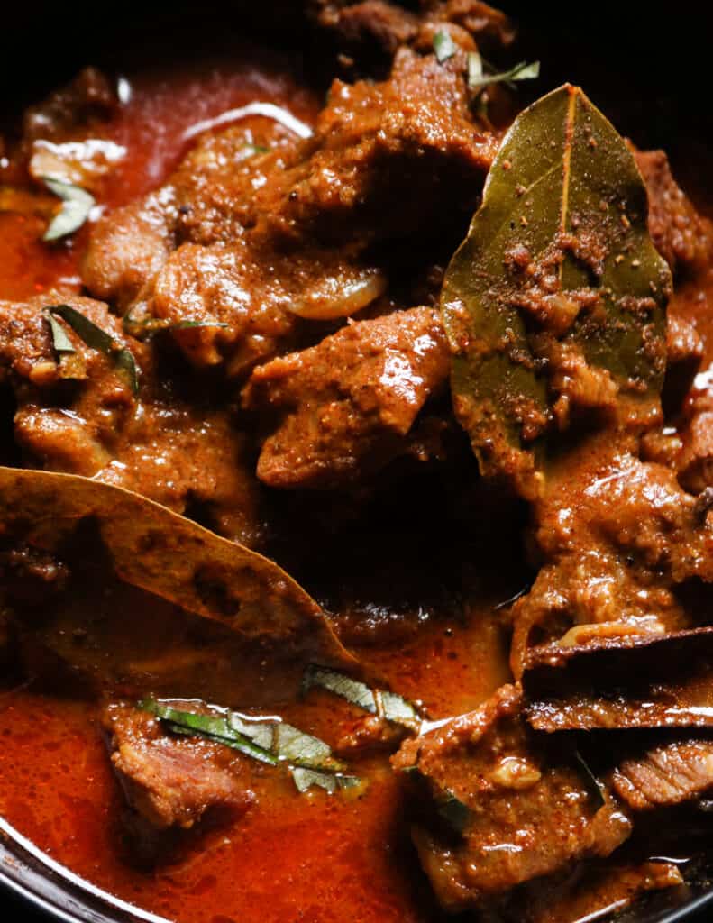 Indian beef curry with bay leaves and cinnamon scooped into a bowl