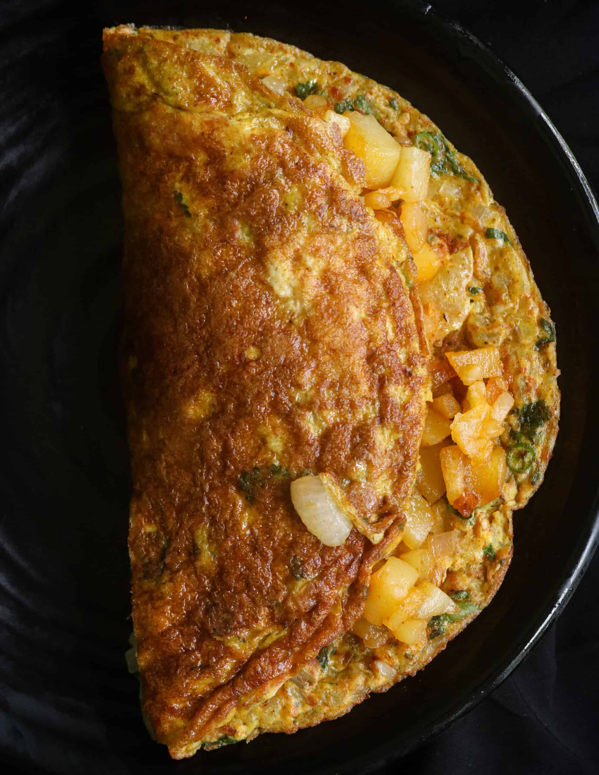 folded omelette stuffed with fried potatoes and served in a black plate.