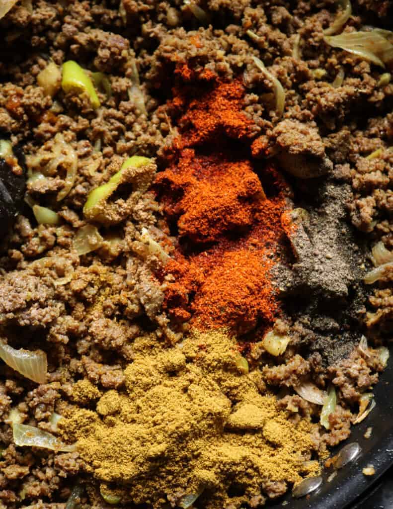adding spice powders to the minced meat with garlic and onions and sliced peppers.