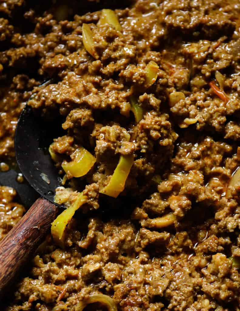 cooked minced curry with peppers and onions served with a wooden spoon.