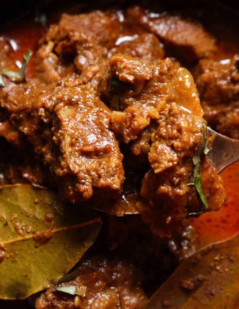 spicy beef curry, beef pieces lifted with a silver spoon.