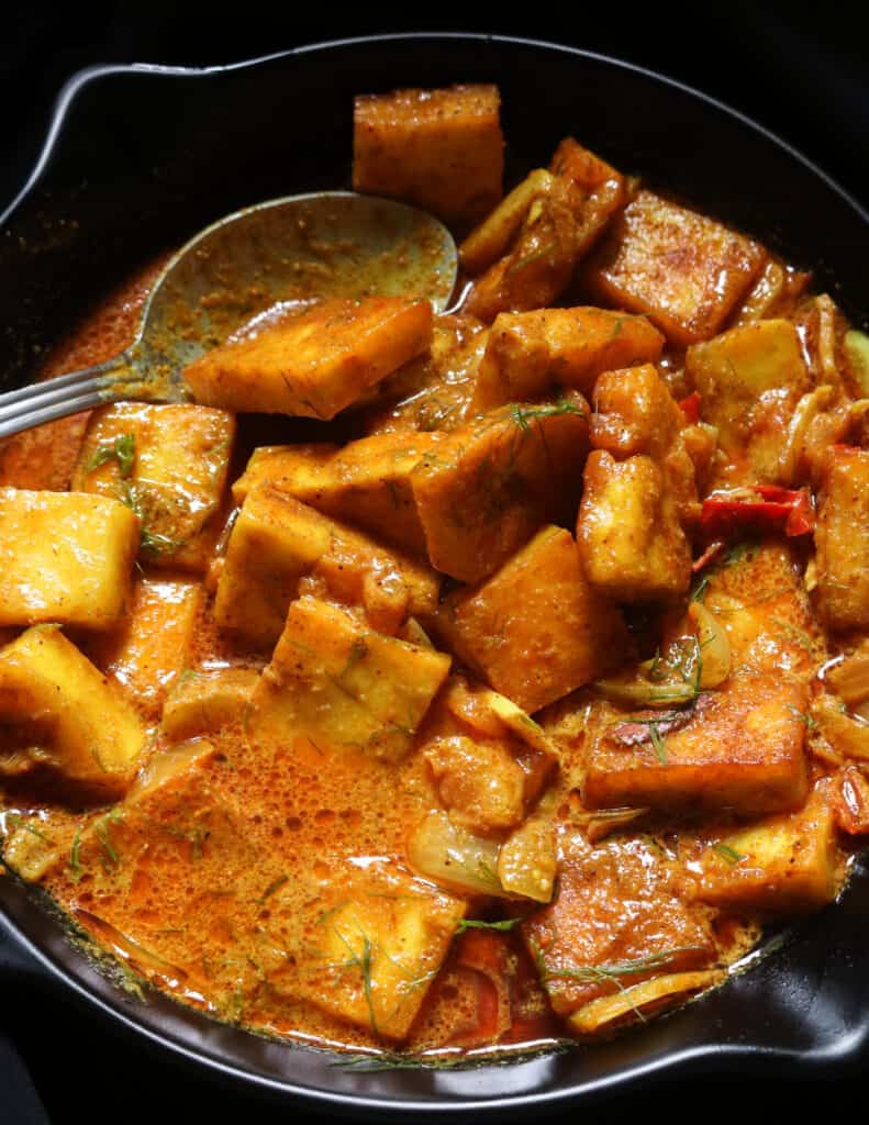 pan of paneer curry cooked in coconut milk with a spoon.