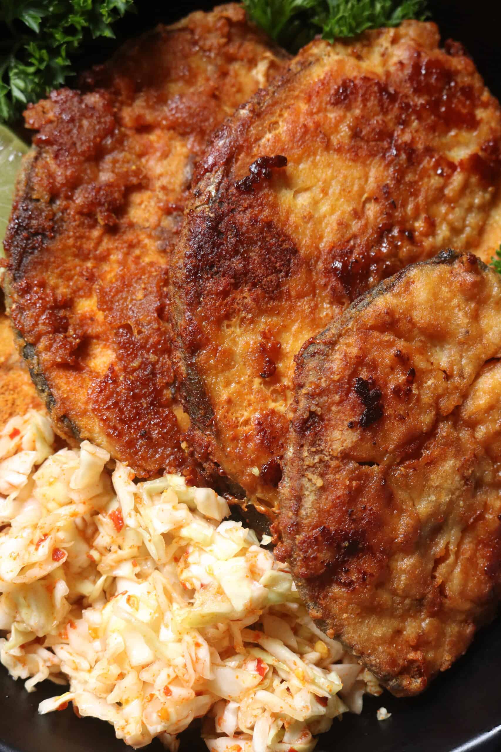 pan fried fish steaks with coleslaw and slices of lime.