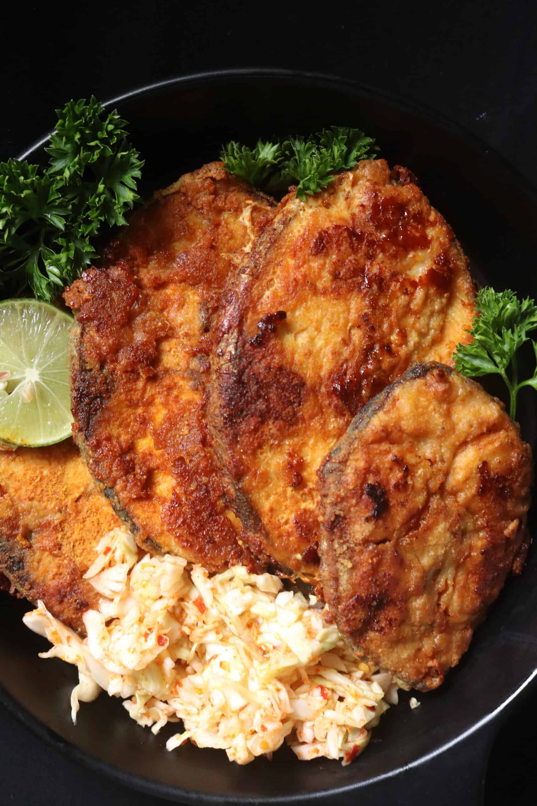 pan fried fish steaks served ina platter with garnishes, lime and coleslaw.