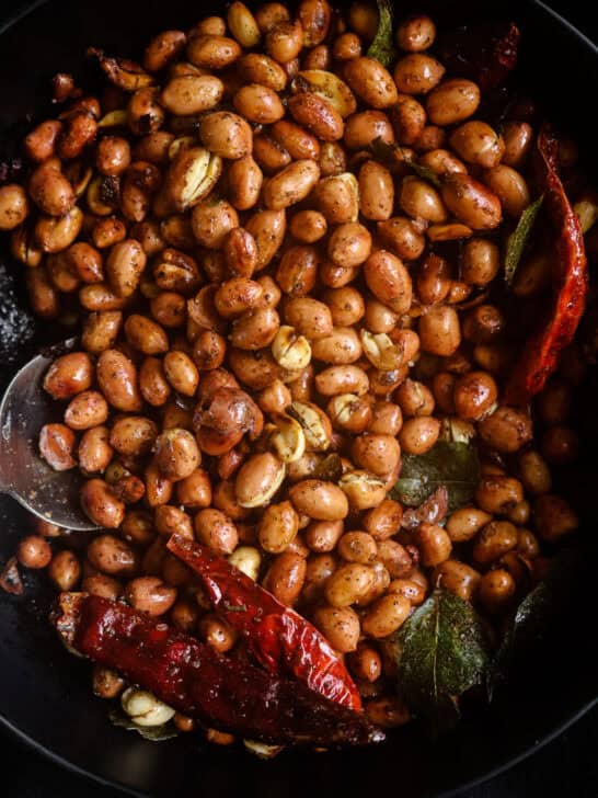 roasted crunchy peanuts served on a bowl with dried red chillies and curry leaves.