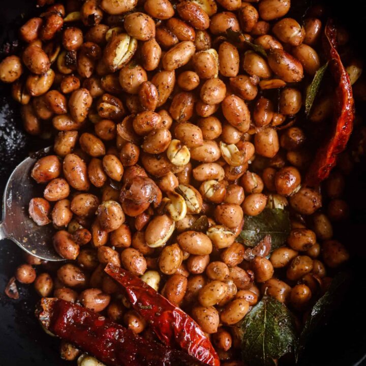 roasted crunchy peanuts served on a bowl with dried red chillies and curry leaves.